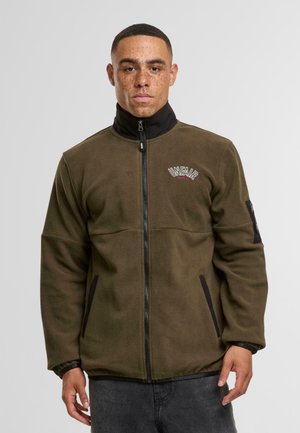 Zelená fleecová bunda s vysokým límcem, černé detaily na zipu a kapsách a vyšitým logem "UNFAIR" na hrudi.