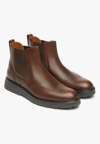 Bruine leren enkellaarzen met elastische zijpanelen, brogue-details op de teen en een zwarte rubberen zool voor verbeterde grip en comfort.