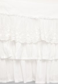Tissu blanc avec une surface texturée, présentant des accents floraux brodés et des couches froncées, créant une apparence douce et superposée.