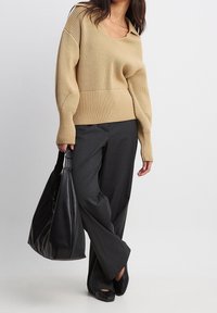 Maglione beige a maglia con scollatura a V e texture a coste, abbinato a pantaloni grigi a gamba larga. Borsa nera oversize e scarpe basse.
