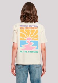 Cremefarbendes Baumwoll-T-Shirt mit einem bunten Grafikdesign auf der Rückseite, das Strahlen, eine Sonne und Text in Lila, Orange, Pink und Grün zeigt. 