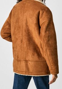 Brun faux suede-jacka med en texturerad finish, som har en fluffig vit foder och en lös, oversized passform. Synliga sömmar och fickor.