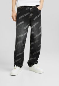 Svarta denimjeans med lös passform, prydda med ett heltryck av "NEW YORK" i vitt, femficksdesign och kontrasterande sömmar.