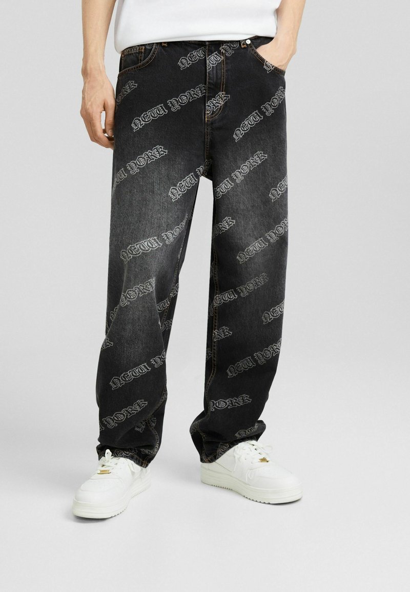 Svarta denimjeans med lös passform, prydda med ett heltryck av "NEW YORK" i vitt, femficksdesign och kontrasterande sömmar.