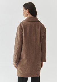 Ruskea herringbone-takki, jossa on leveä kaulus, rento istuvuus ja pitkät hihat, valmistettu teksturoidusta kankaasta, suora selkäosa ja sivutaskut.