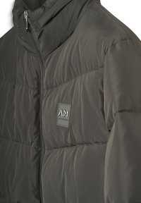 Donkergrijze gewatteerde jas met een hoge kraag, rits aan de voorkant en een klein rechthoekig logopatch op de borst.