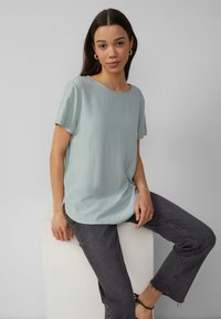 Himmelbluse mit kurzen Ärmeln und rundem Ausschnitt, glatter Textur und lockerer Passform, kombiniert mit dunkelgrauen, cropped Jeans.