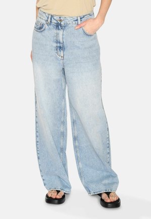Ljusblå vida jeans i denim, med hög midja, framfickor och lätt blekning. Bärs med svarta sandaler.