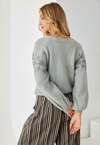Suéter de punto gris suave con patrón texturizado y bordado floral en las mangas, combinado con pantalones de pierna ancha a rayas.
