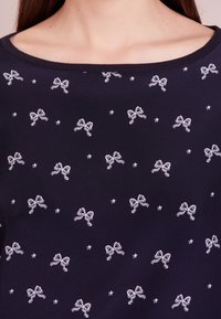 Top navy con motivi stampati di archi e stelle ricamate in bianco, scollatura rotonda e texture morbida. Il design presenta motivi ripetuti.