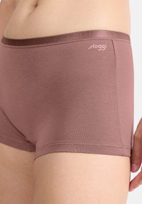 Lyhyet rose-väriset alushousut, jotka on valmistettu sileästä kankaasta. Ne ovat varustettu pehmeällä vyötäröosalla, jossa on logodetaili, ja ne esittelevät muotoilevaa designia sekä saumatonta reunustusta.