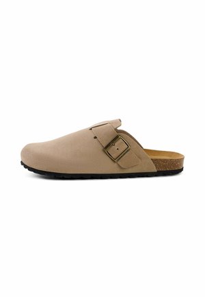 Beige ruskind slip-on træsko med justerbar messing spænde, korksål og tekstureret sort gummisål, vist fra siden på hvid baggrund.