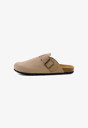 Beige ruskind slip-on træsko med justerbar messing spænde, korksål og tekstureret sort gummisål, vist fra siden på hvid baggrund.