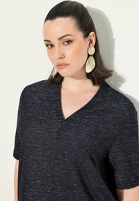 Granatowa bluzka z dekoltem w serek i krótkimi rękawami, o fakturowanym paskowanym wzorze. Duże kremowe kolczyki-statement dopełniają całość.
