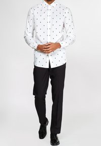 Weißes Langarmhemd mit kleinen grünen Baum-Mustern, zugeknöpft, kombiniert mit schwarzen Hosen und schwarzen Dressschuhen. Glatte Stofftextur.