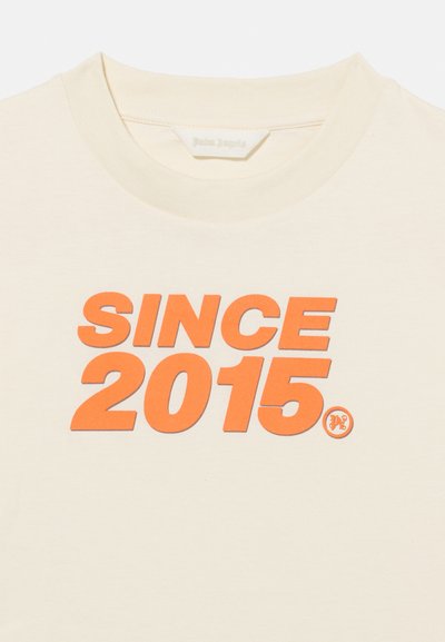 Κρεμ χρώματος μπλουζάκι με στρογγυλή λαιμόκοψη και έντονο πορτοκαλί κείμενο "SINCE 2015" τυπωμένο στο κέντρο μπροστά.