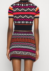 Neulemekko, jossa on lyhyet hihat ja vartalonmyötäinen yläosa. Kuvioitu mustana, vaaleanpunaisena, oranssina ja valkoisena geometrisilla kuoseilla ja resoripalkeilla.