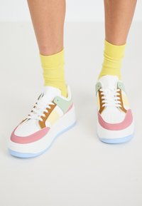 Baskets blanches avec des accents pastel en menthe, rose et jaune. Présentent une semelle épaisse, un nez perforé et des lacets contrastés.