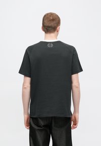 Fekete, puha pamutból készült póló, rövid ujjakkal, kerek nyakkivágással és egy kis kör alakú logóval a hát felső részén.