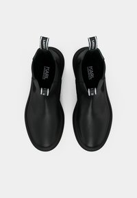 Une paire de bottes noires en cuir Karl Lagerfeld �à enfiler avec des languettes sur un fond blanc, vues de dessus.