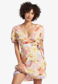 Vestido envolvente floral en colores pastel con mangas abullonadas, escote en V profundo y lazo lateral, confeccionado en una tela ligera y con un patrón texturizado.