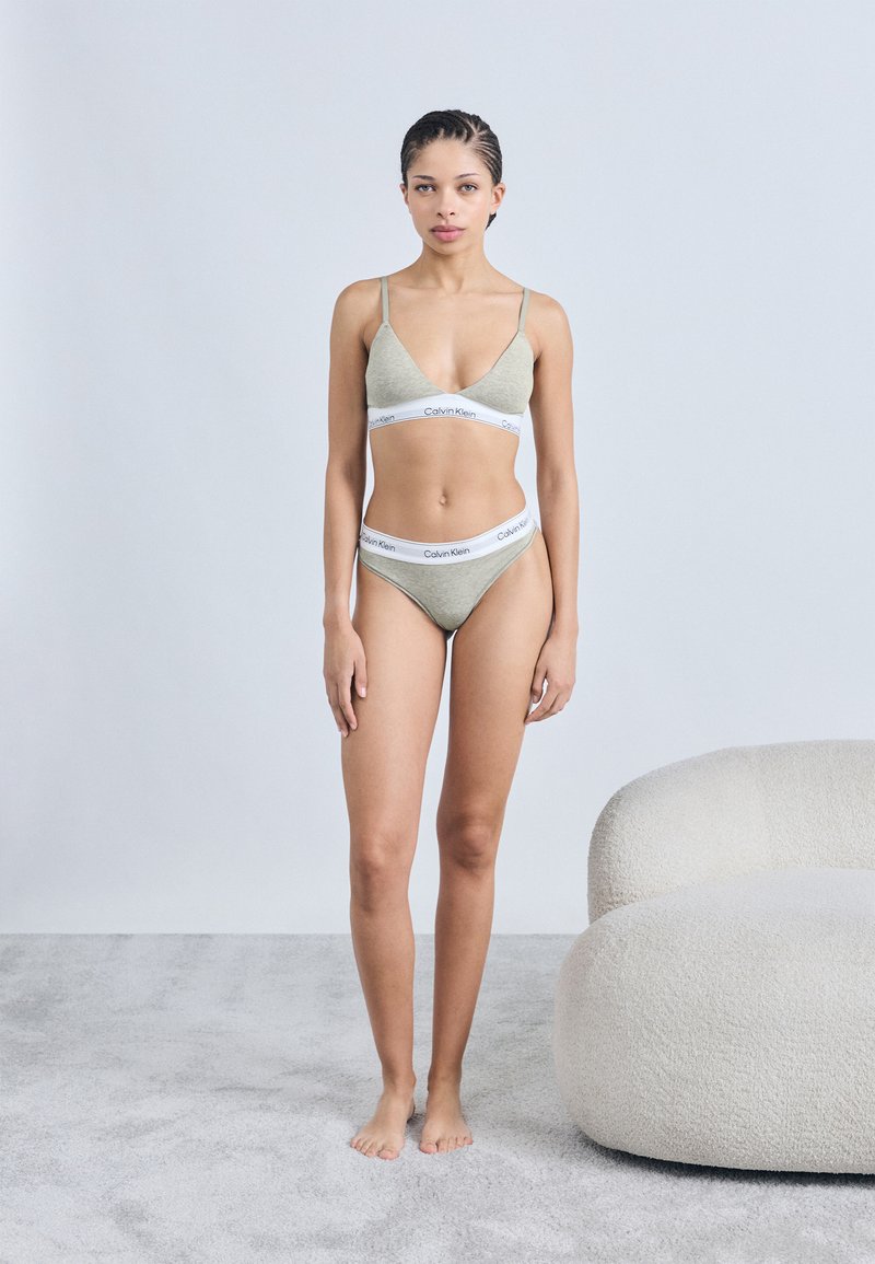 Σετ γκρι βραλέτα και μπικίνι με λευκή λωρίδα λογαριασμού Calvin Klein. Μαλακό ύφασμα, τριγωνικός σχεδιασμός σουτιέν και μινιμαλιστικό στυλ.