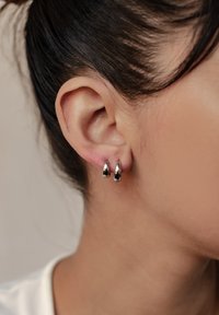 Silberne Creolen mit einer glänzenden, glatten Oberfläche, die ein rundes Design und eine subtile Kurve aufweisen, werden an den Ohren eines Models präsentiert.