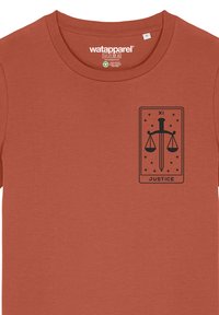 Ein rustfarbenes T-Shirt aus weichem Stoff mit einem schwarzen Grafikdesign, das ein Schwert und Waagen innerhalb eines umrandeten Designs zeigt, das mit "GERECHTIGKEIT" und "XI" beschriftet ist.