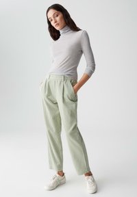 Grauer Langarmrollkragenpullover kombiniert mit hellgrünen, strukturierten, plissierten Hosen und weißen Sneakern. Minimalistisches Design mit Taschen.