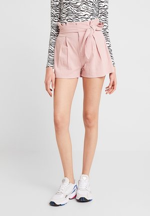 Shorts roses taille haute avec une ceinture nouée, des plis à l'avant et un tissu texturé. Associés à des baskets blanches et un haut à rayures noir et blanc.