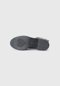 Black sandal sole with textured surface and heart-shaped tread. Features engraved brand name “LOVE MOSCHINO” near heel.