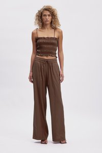 Hnedý zúžený crop top s volánikmi, spojený s voľnými hnedými širokými nohavicami so sťahovacím pásom. Jednoduchá, prirodzená textúra látky.