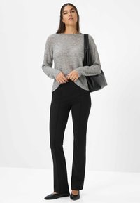 Lichtgrijze gestructureerde trui met ribbels aan de mouwen, gecombineerd met zwarte slim-fit broek en zwarte ballerina's, aangevuld met een zwarte schoudertas.