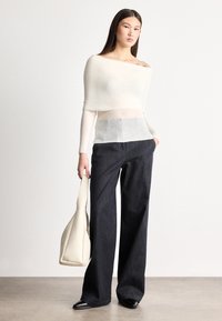 Ľahký, smotanovo biely pletený top s dlhými rukávmi; priehľadný stredný diel. Kombinovaný s vysokým pásom, tmavomodrými džínsami s širokými nohavicami; hladká textúra.