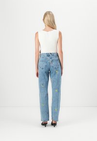Lichtblauwe denim jeans met geborduurde zon- en maanontwerpen, met een rechte pijp en een hoge taille. Gepaarde met een wit geribbeld tanktop.