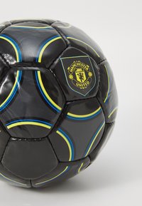Čierny futbal s žltými a modrými akcentmi, s textúrovaným povrchom a výrazne zobrazeným emblémom Manchester United.