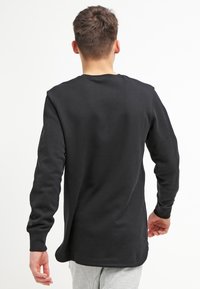 Svart långärmad tröja med avslappnad passform, rund halsringning och sidofickor. Tillverkad av mjukt material med ribbade ärmslut och fåll.