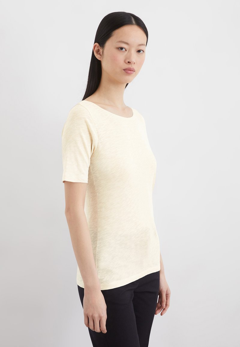 Helles Gelb, enganliegendes Kurzarmoberteil aus einem weichen, strukturierten Stoff. Verfügt über einen Rundhalsausschnitt und einen geraden Saum. Getragen mit schwarzen Hosen.