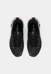 Ζευγάρι μαύρων αθλητικών παπουτσιών Nike Free με λευκό σπαστό σχέδιο και μπεζ σόλες, απεικονισμένα από ψηλά σε λευκό φόντο.