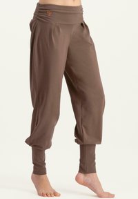 Braune, locker sitzende Hose mit einem breiten, gerafften Taillenbund. Hergestellt aus weichem Stoff, mit schmal zulaufenden Säumen und dezenter Logodetail am Taillenbund.