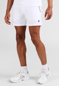 Pantaloni sportivi bianchi in tessuto leggero con una vestibilità aderente. Presentano un piccolo logo Fila e una sottile bordatura nera sui lati.
