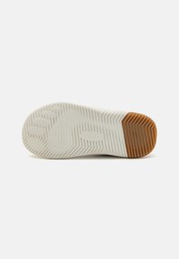 Hvit sneakersåle med teksturert gummioverflate, med horisontale spor og en brun gummihæl for bedre grep og holdbarhet.