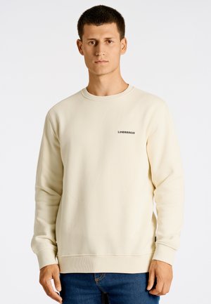 Felpa beige con maniche lunghe e polsini a coste. Presenta un collo a giro e una piccola scritta nera "LINDENBRGH" sul petto. Tessuto morbido.