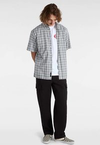 Kortærmet ternet skjorte i sort, hvid og grå, lagt over en hvid T-shirt, kombineret med sorte cargobukser og ternede slip-on sko.