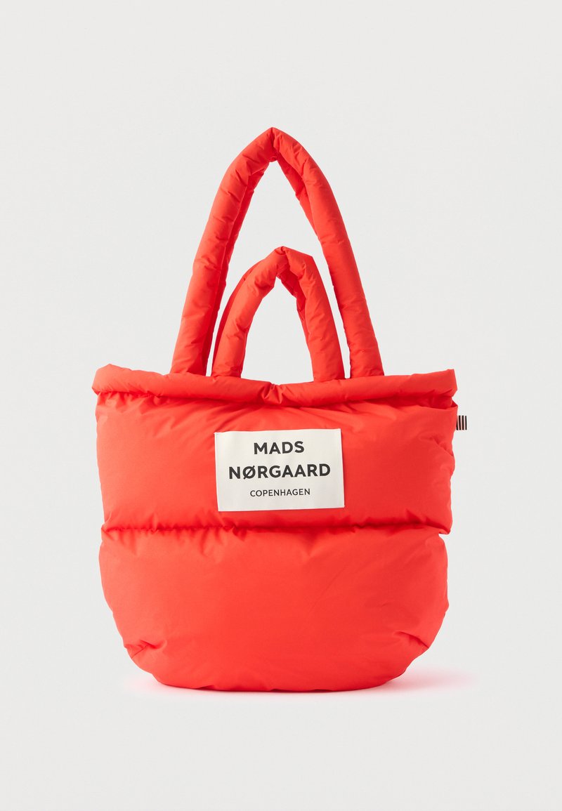 Κόκκινη επενδυμένη τσάντα ώμου με δύο χερούλια και μια λευκή ετικέτα στη μπροστινή πλευρά που γράφει "Mads Nørgaard Copenhagen".