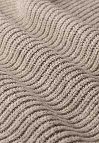 Tejido de punto beige con una textura ondulada, que presenta patrones de costilla elevados y un hilo suave y grueso. Apariencia uniforme y consistente en todo.
