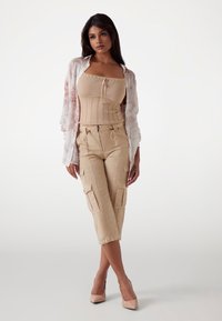 Beige geripptes Korsettoberteil, blumenverziertes durchsichtiges Hemd und beige Cargo-Hosen mit Taschen und Kordelzügen. Kombiniert mit hautfarbenen High Heels.
