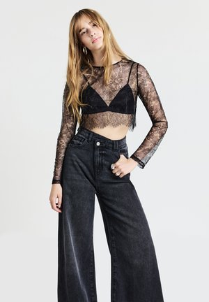 Cropped top nero in pizzo a maniche lunghe con dettagli trasparenti e orlo scallop abbinato a jeans in denim neri a vita alta e gamba larga.