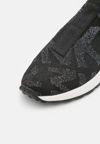 Baskets noires avec un dessus en tricot texturé présentant un motif subtil, une semelle blanche et une languette en tissu noir avec un détail de logo.