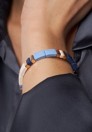 Bracelet coloré avec des maillons rectangulaires et triangulaires en bleu, crème et bleu foncé avec des accents dorés. Texture lisse, design moderne.